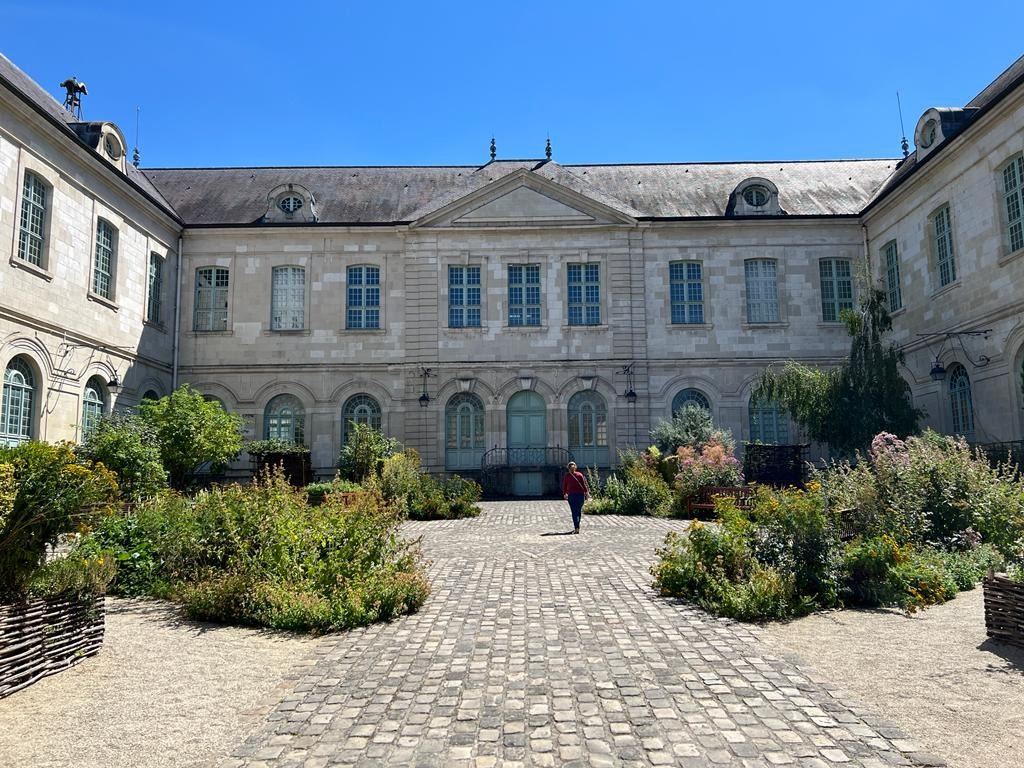 A classical courtyard of an elegant stone building with manicured gardens and arched windows under clear blue sky.
