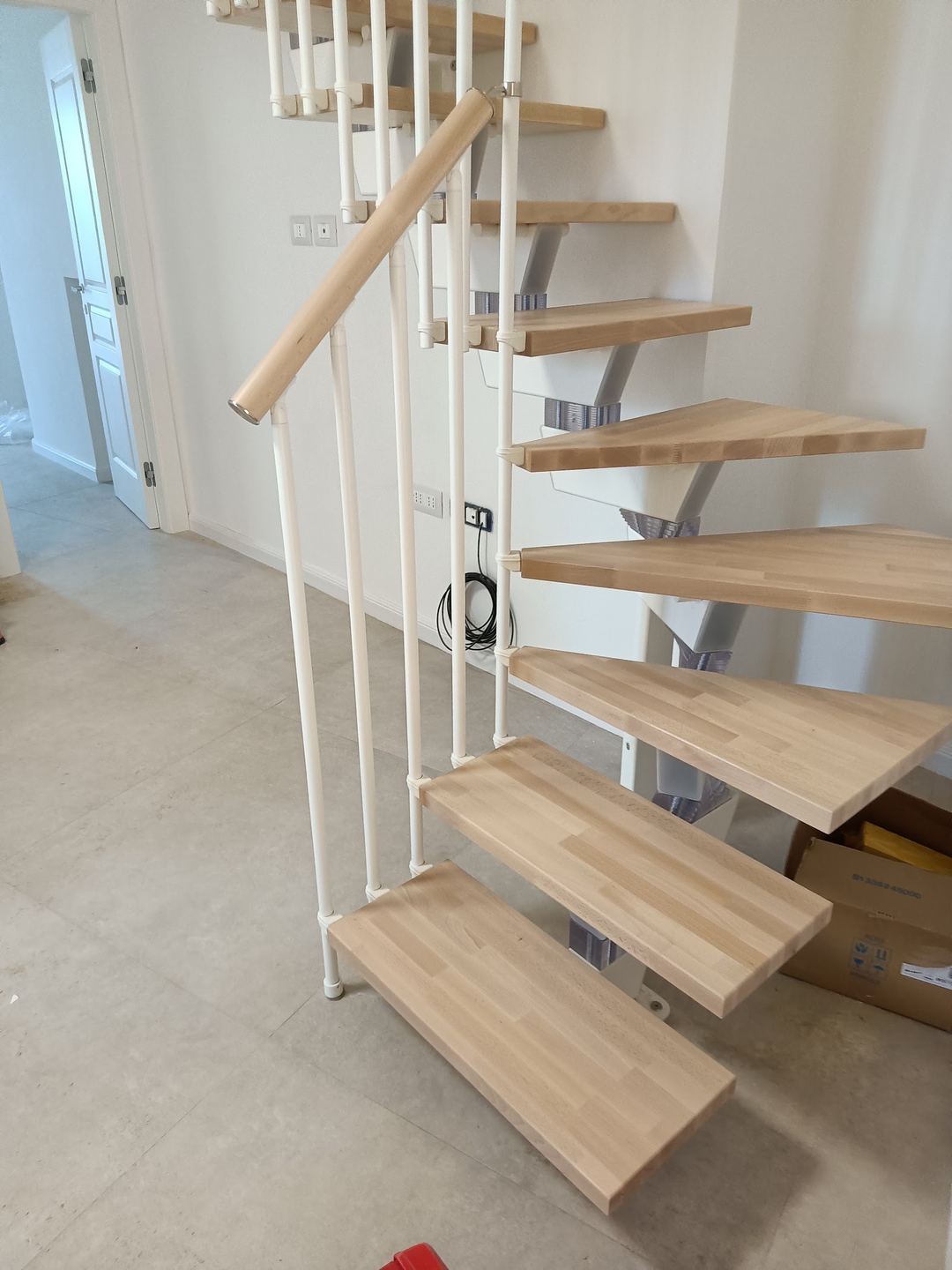 A modern spiral staircase with wooden steps and white metal frame under construction in an interior space.